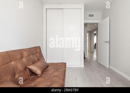 Room with brown leather folding sofa bed and a built-in wardrobe with white sliding doors Stock Photo