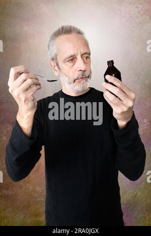 A mature man is pouring cough syrup in a spoon to cure his sore throat and bronchitis Stock Photo