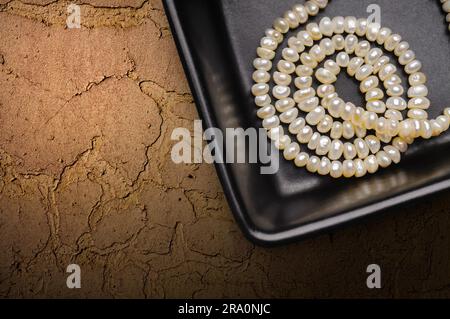 natural pearls necklace in a little black ceramic cup on a textured background with space for copy text 2ra0njc
