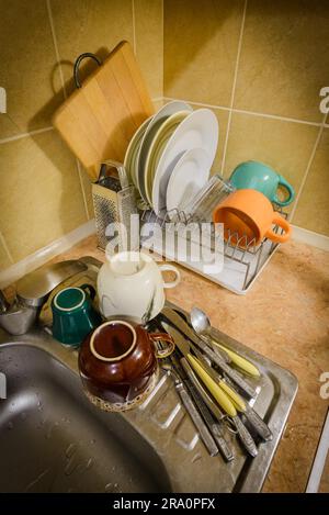 Dishes, cups, glasses, plates, forks, knives and spoons are drying close to the sink, after they have been washed in kitchen Stock Photo