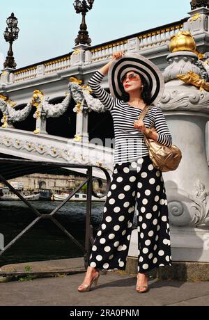 An glamorous Asian woman in Paris modelling beside Pont Alexandre III wearing a striped Breton tee shirt and polka dots culottes. Stock Photo