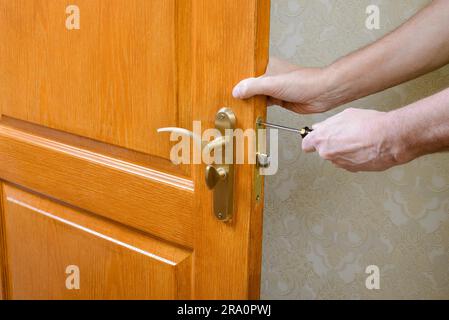 A man is mounting the protection strike of the deadbolt on a door with a classical curved style bronze handle using a screwdriver Stock Photo