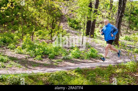 A senior man dressed in black and blue is running in the forest, during a nice autumn day. Motion blur effect due to the speed. The background is Stock Photo