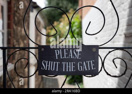 Polite notice reminding people to shut the gate mounted on an ornate metal gate. Stock Photo