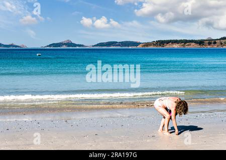 Blonde woman with curly hair catching shells on a Galician beach Stock Photo