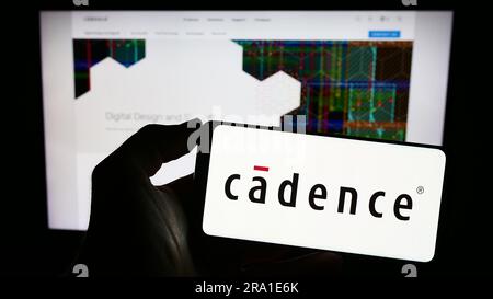 Person holding cellphone with logo of US software company Cadence Design Systems Inc. on screen in front of webpage. Focus on phone display. Stock Photo