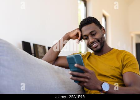 Happy african american man using smartphone in living room Stock Photo
