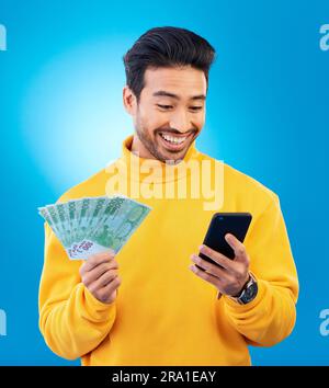 Man, phone and money in studio with prize, esports gambling or happy for success by blue background. Young asian guy, student and smartphone with cash Stock Photo