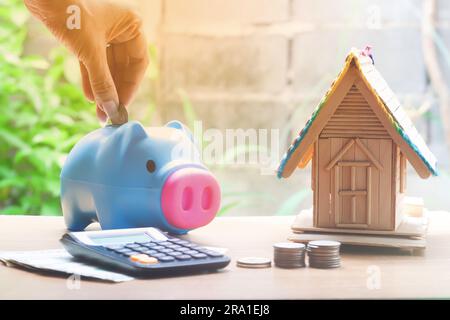 Woman hand put coin in piggy bank with coin stacks and house model, savings plans for housing Stock Photo
