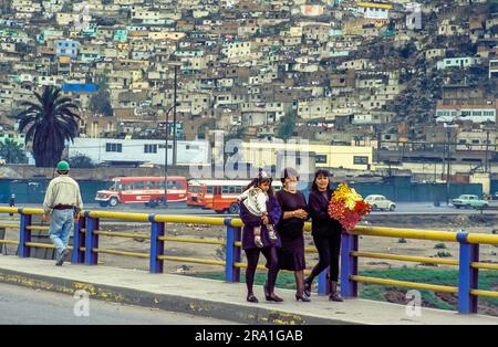 Peru, Lima; Women going to a party. In the background one of the  slums in Lima. Stock Photo