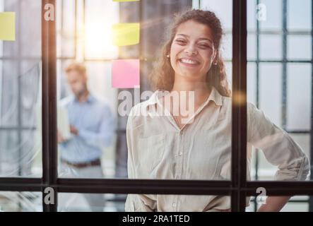 Bringing her vision to life. Shot of a confident businesswoman presenting an idea to her colleague using adhesive notes on a glass wall in the office. Stock Photo