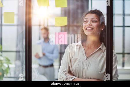 Bringing her vision to life. Shot of a confident businesswoman presenting an idea to her colleague using adhesive notes on a glass wall in the office. Stock Photo