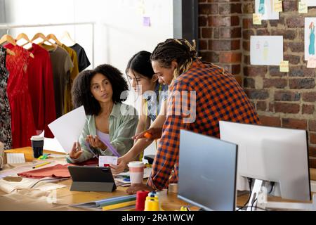 Diverse fashion designers sitting at desk, using tablet and discussing work at office Stock Photo
