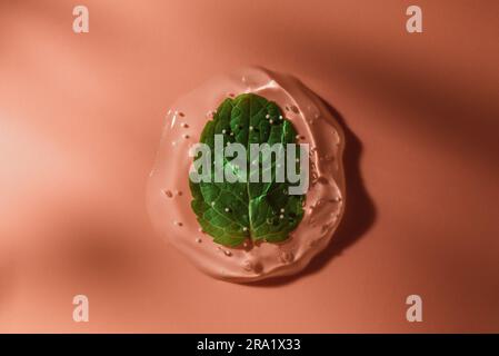 A drop of cosmetic gel with mint leaf on a pink background in the rays of the sun. Stock Photo