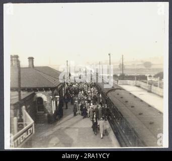 Two snapshot views of Butterley, an old crowded railway station platform in the 1920s, showing people waiting to traval to a tennis match. Advertising signs, fashion, also shows the photographer with his tripod mounted camera.  Very atmospheric. Stock Photo