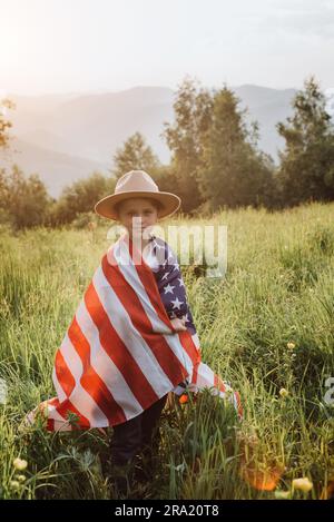 Portrait of cute smiling little girl child in hat celebrating on July, 4 Independence Day of USA during sunset in beautiful summer mountains. Adorable Stock Photo