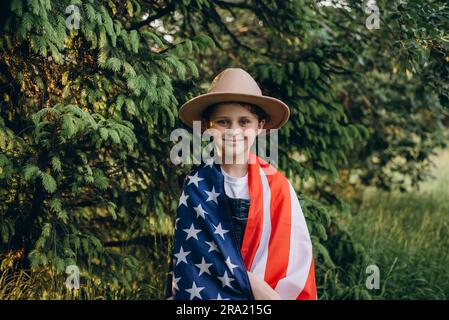 Portrait of smiling little girl in hat celebrating on July, 4 Independence Day of USA at sunny day. Pretty child with american flag of United States. Stock Photo