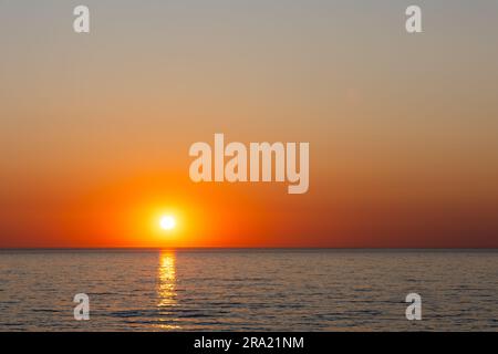 A large orange sun setting over a calm sea. Static shot taken during a cloudless evening Stock Photo