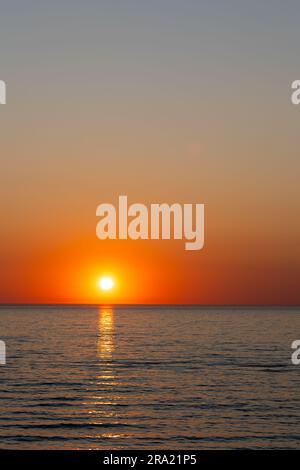 A large orange sun setting over a calm sea. Static shot taken during a cloudless evening Stock Photo