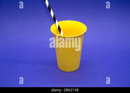 Bright Yellow plastic drinking cup on a Blue Background with striped drinking straw Stock Photo