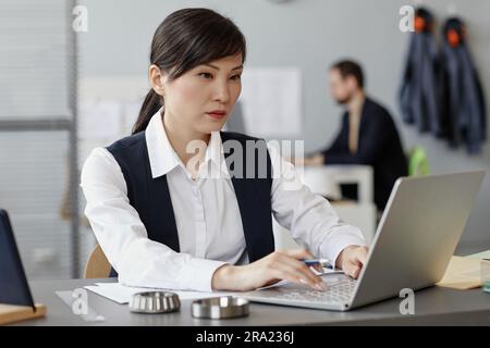 Portrait of young Asian woman as female engineer using laptop at workplace in office Stock Photo