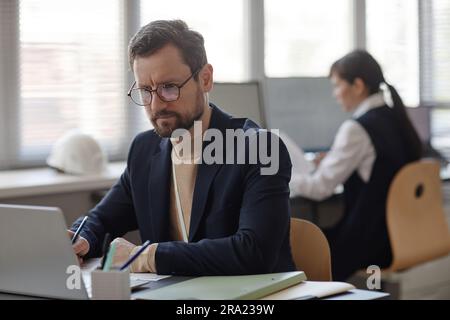 Portrait of bearded adult man wearing glasses using laptop while working in office Stock Photo