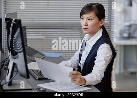 Side view portrait of Asian woman as female engineer using computer and blueprints in office Stock Photo