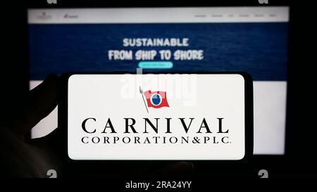 Person holding smartphone with logo of cruise company Carnival Corporation plc on screen in front of website. Focus on phone display. Stock Photo
