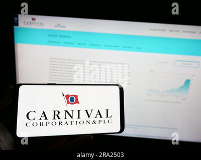 Person holding mobile phone with logo of cruise company Carnival Corporation plc on screen in front of business web page. Focus on phone display. Stock Photo