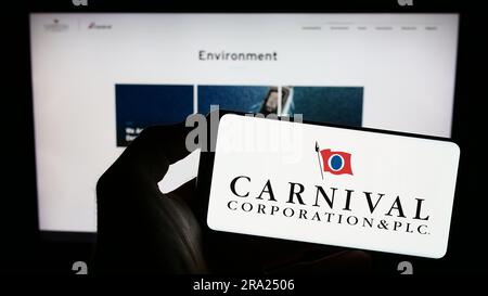 Person holding cellphone with logo of cruise company Carnival Corporation plc on screen in front of business webpage. Focus on phone display. Stock Photo