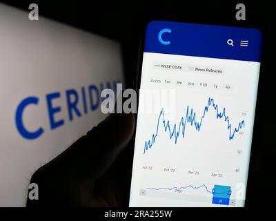 Person holding cellphone with website of US software company Ceridian HCM Holding Inc. on screen with logo. Focus on center of phone display. Stock Photo