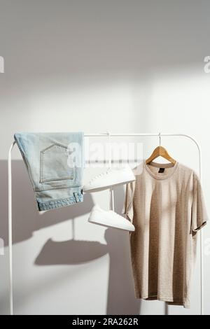 Mens beige t-shirt, denim shorts and white sneakers displayed on white clothes rack. Stock Photo