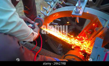 Worker Using Angle Grinder in Agriculture and throwing sparks, Industry worker cutting metal with grinder. Lots of glowing sparks Stock Photo