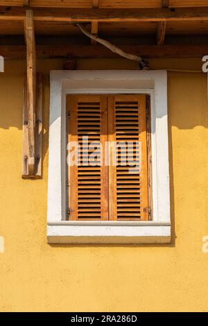 Window with closed wooden shutters on the yellow facade of the house. Stock Photo