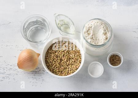 Ingredients: green lentils, onions, flour, water, vegetable oil, salt and pepper on a light blue background, top view. Cooking delicious vegan food. Stock Photo