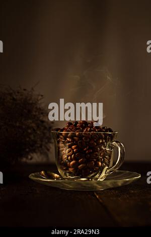 Coffee beans in a transparent cup on a wooden table and smoke over the cup Stock Photo