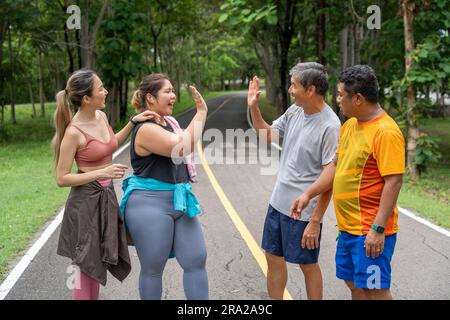 A group of 2 male and 2 female runners giving each other high five to celebrate their running success at a running track of a local park Stock Photo