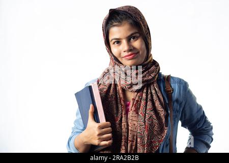 A pretty young Indian girl with books in hand and backpack pointing ...