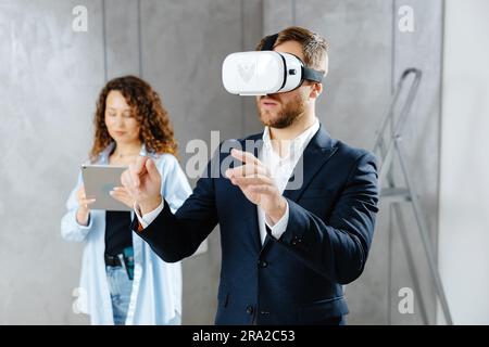 Man client wearing VR glasses imagining future interior standing with designer at the construction site. The concept of repair on a modern design Stock Photo