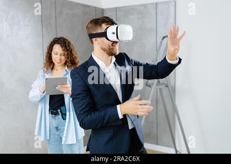 Man client wearing VR glasses imagining future interior standing with designer at the construction site. The concept of repair on a modern design Stock Photo