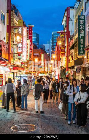 Chinatown in Kobe at night. View along narrow pedestrian street filled with people wandering between food stalls selling takeaway Chinese cuisine. Stock Photo