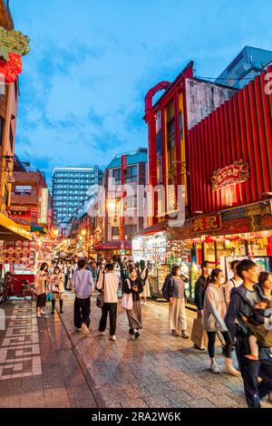 Chinatown in Kobe at night. View along narrow pedestrian street filled with people wandering between food stalls selling takeaway Chinese cuisine. Stock Photo