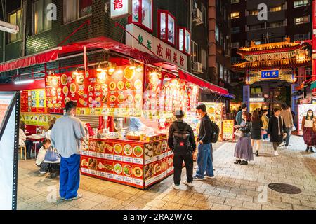 Large corner stall selling Chinese fast-food including steamed buns and dumplings, outside a restaurant by the Eastern Gate, Chinatown in Kobe. Night. Stock Photo