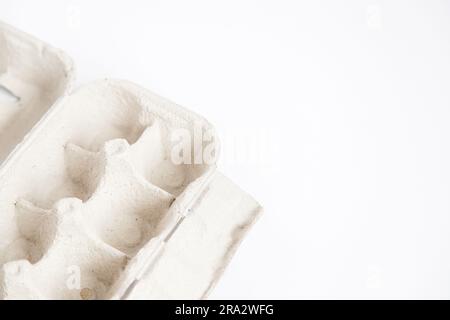 Detail of empty and open recycled cardboard egg carton in the corner of the image on a white background. Close up and copy space. Stock Photo