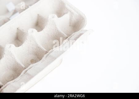 Detail of empty and open recycled cardboard egg carton in the corner of the image on a white background. Close up and copy space. Stock Photo