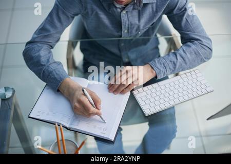 pensive male entrepreneur coming up with idea while taking notes writing down important thoughts sitting at workplace Stock Photo