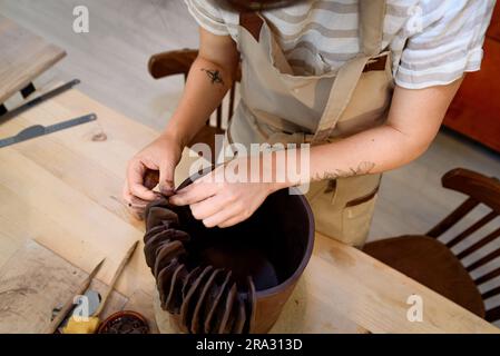 Woman in pottery workshop working raw ceramic vase and clay to make pot. Pottery workshop with natural light scraping, smoothing, shaping and sculptin Stock Photo