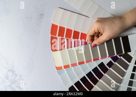 Female hand holding color palette guide catalog with colour swatches. Architect or home interior design, flat lay composition with copy space. Stock Photo