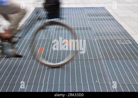 New ventilation iron grid in an urban area with a cyclist passing. Stock Photo