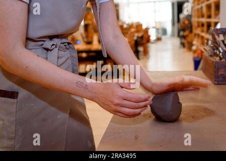woman hands working raw clay dough ball in pottery workshop working raw ceramic vase and clay to make pot. Pottery workshop with natural light scrapin Stock Photo
